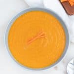 spicy carrot soup in blue bowl against white background with cutting board in the background