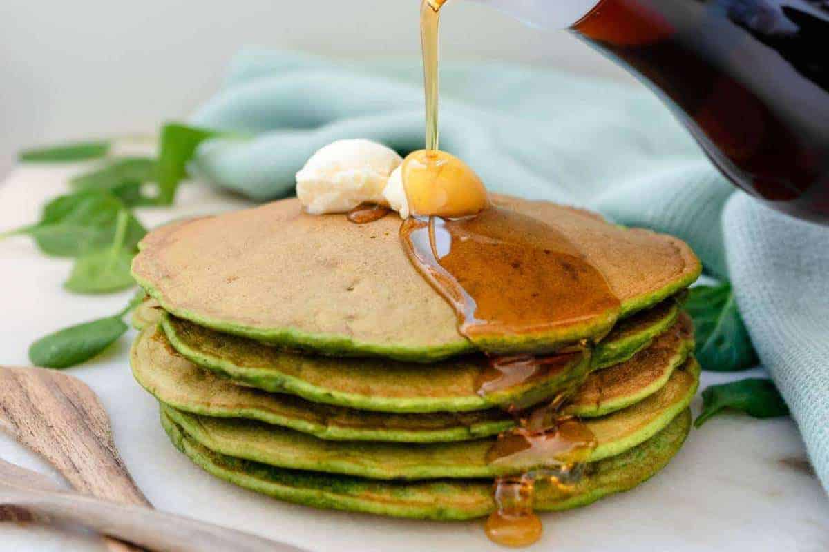 Syrup being drizzled over a stack of spinach banana pancakes.