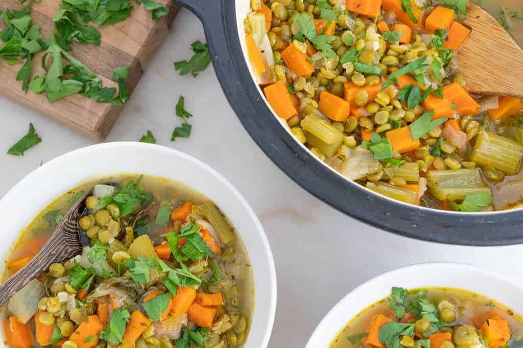 Close up of two bowls and a pot of split pea soup with carrots and celery.
