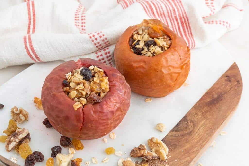two stuffed baked apples on a white cutting board