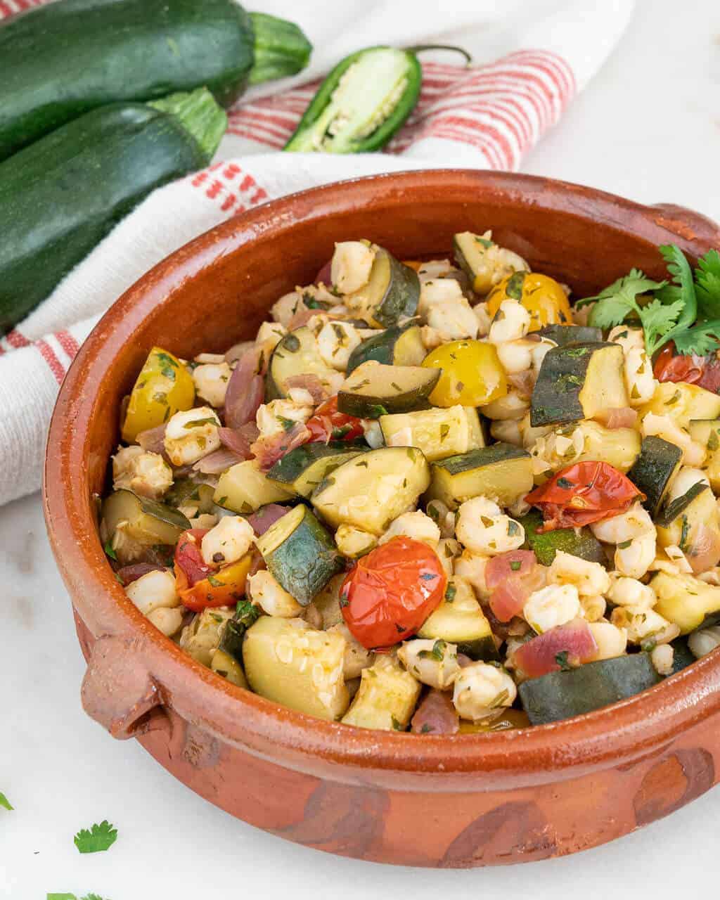 Summer zucchini and hominy salad in a brown serving bowl.