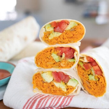 Sweet Potato Burritos stacked on a white and red towel with ingredients in the background