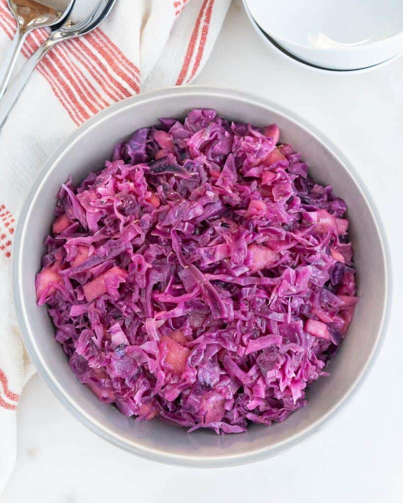 finished dish of red cabbage with apples in a white bowl against a white background
