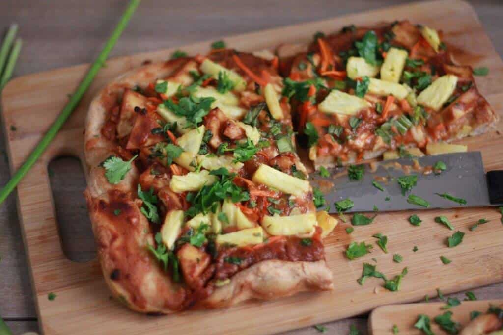 Thai-inspired pizza on a wood board with a chef's knife.