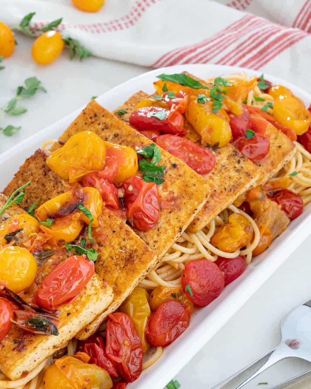 Tofu filets over a bed of tomatoes and pasta.