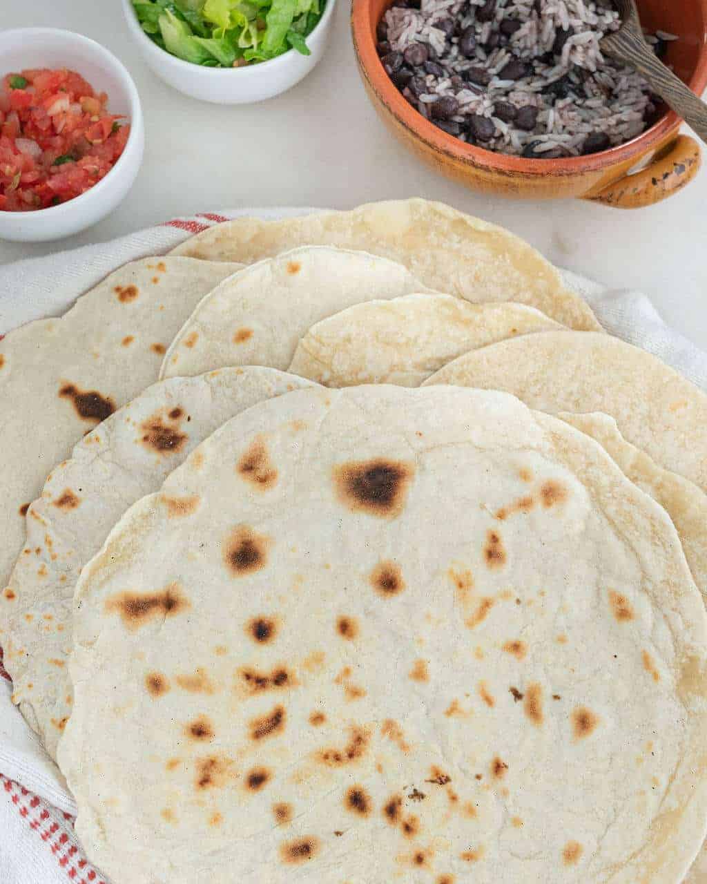 Handmade flour tortillas in a stack on a white towel.