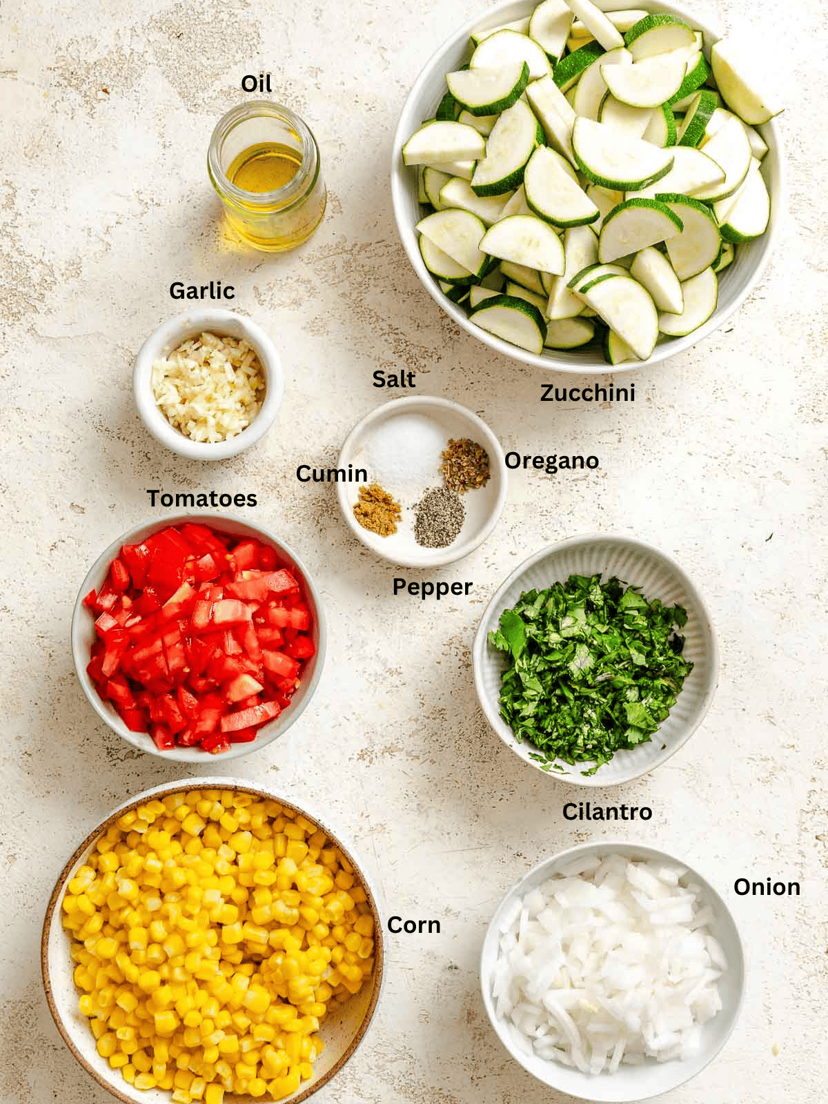 Ingredients for Easy Calabacitas Recipe (Mexican Zucchini) measured out on a white surface.