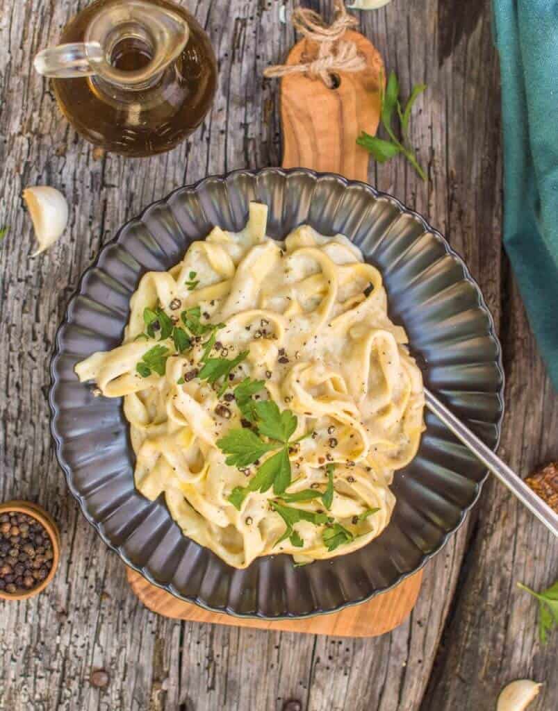 finished Vegan Fettuccini Alfredo plated on a dark plate against a dark wooden background