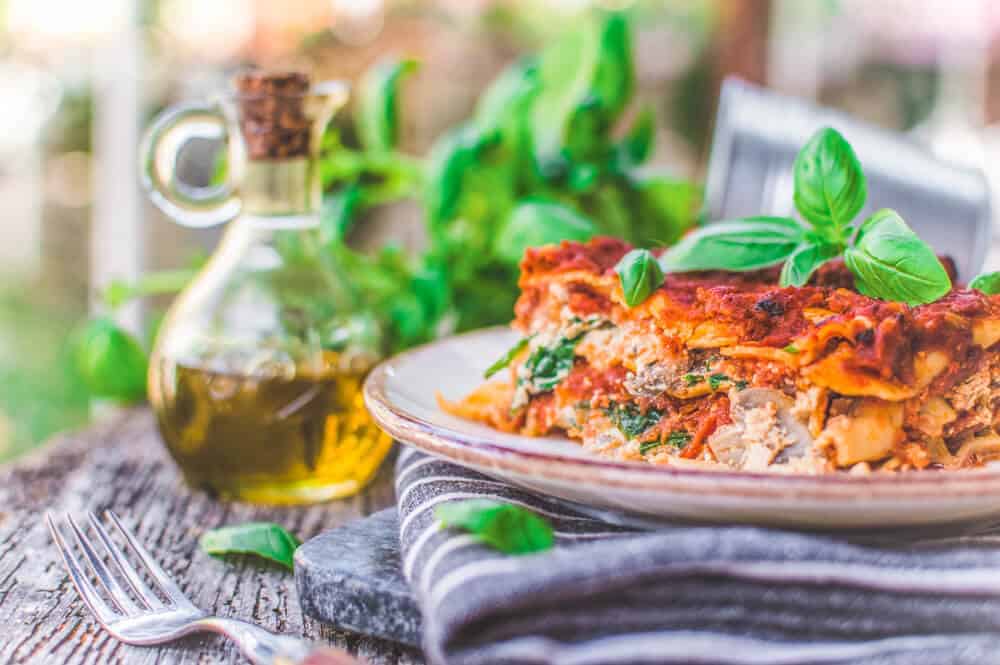 Finished Vegan Lasagna With Tofu Ricotta plated on a gray towel with ingredients in the background