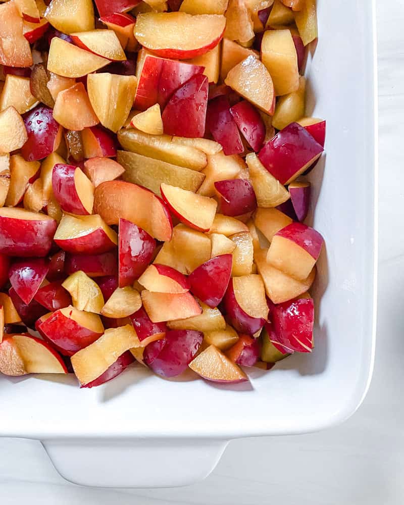 Process shot showing cut plums in baking dish.