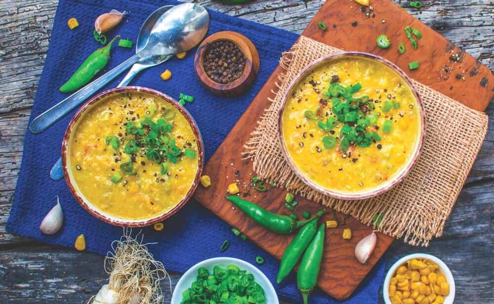 two bowls of corn chowder side by side on a table with a blue tablecloth