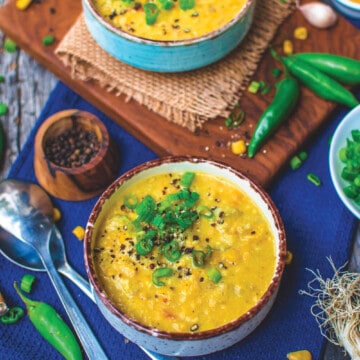 two bowls of corn chowder against a blue place mat with ingredients in the background