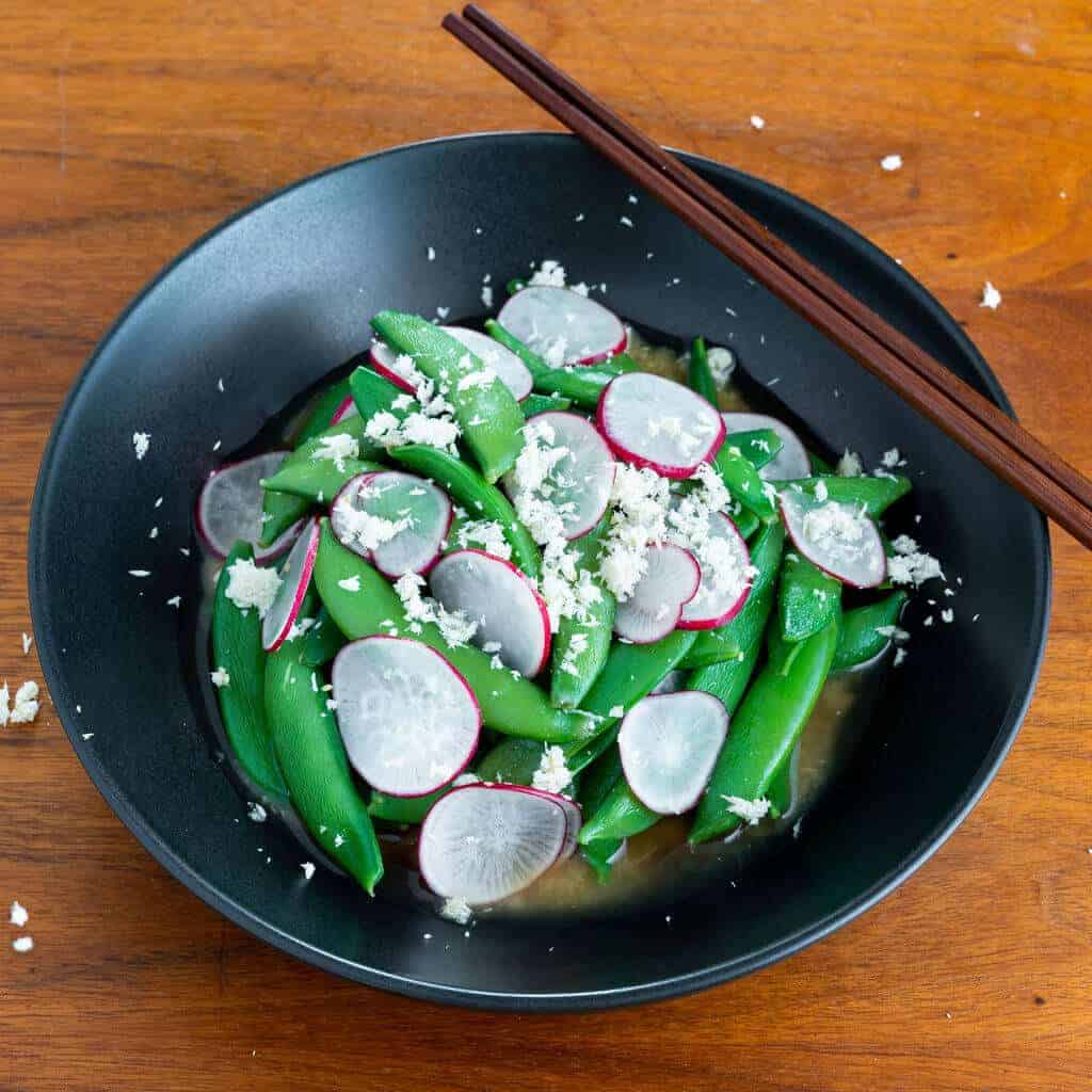 Miso glazed snap peas in a bowl with thin radishes.