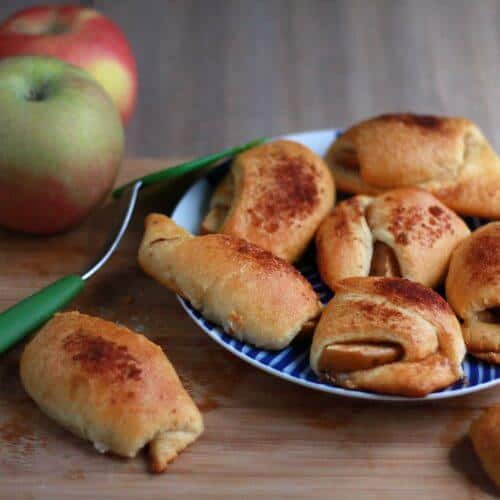 Apple crescent rolls piled on a plate next to a bowl of apples.