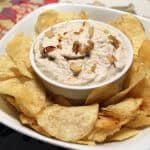 Chips around a bowl of vegan french onion dip.