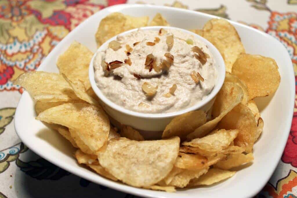 cashew french onion dip in a white bowl on top of a palte with chips