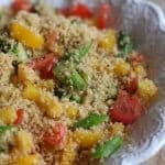 Couscous and brightly colored bell peppers in a white serving bowl.