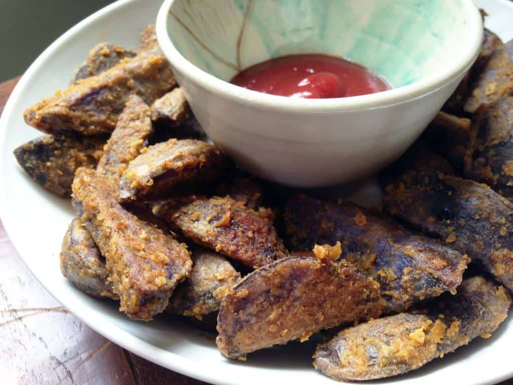Crispy purple potato wedges arranged with a small bowl of ketchup.