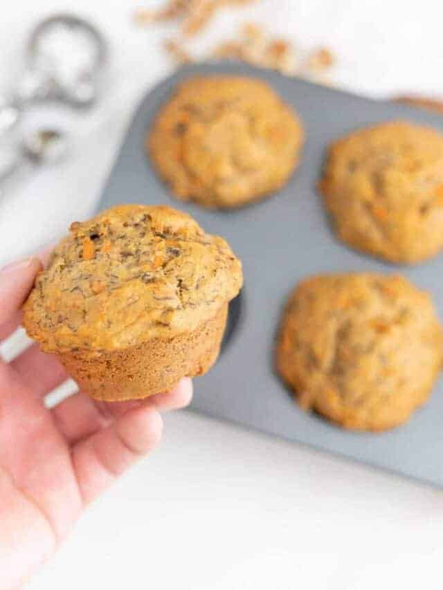 A hand holding a carrot muffin over the muffin tin.