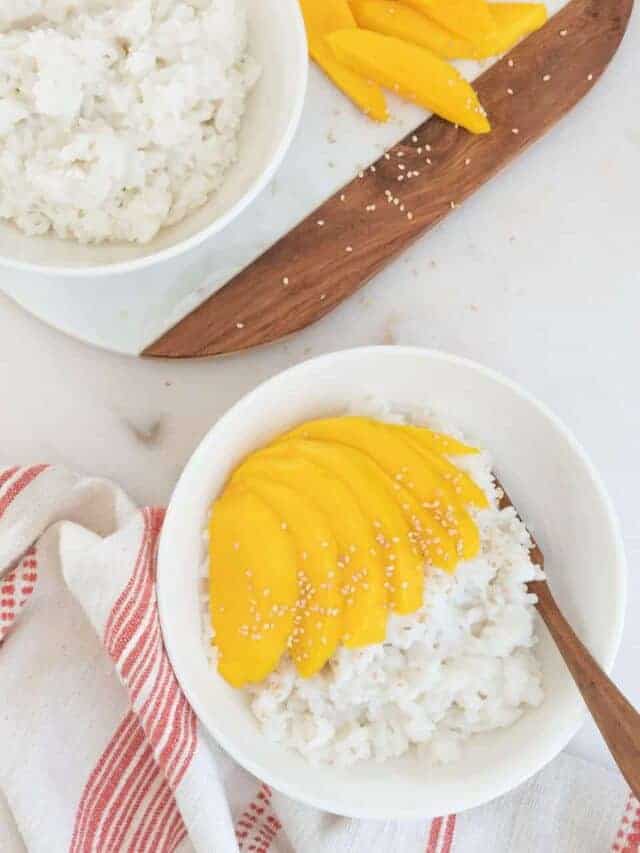 completed mango sticky rice in a white bowl with a bowl of rice and mangos in the background