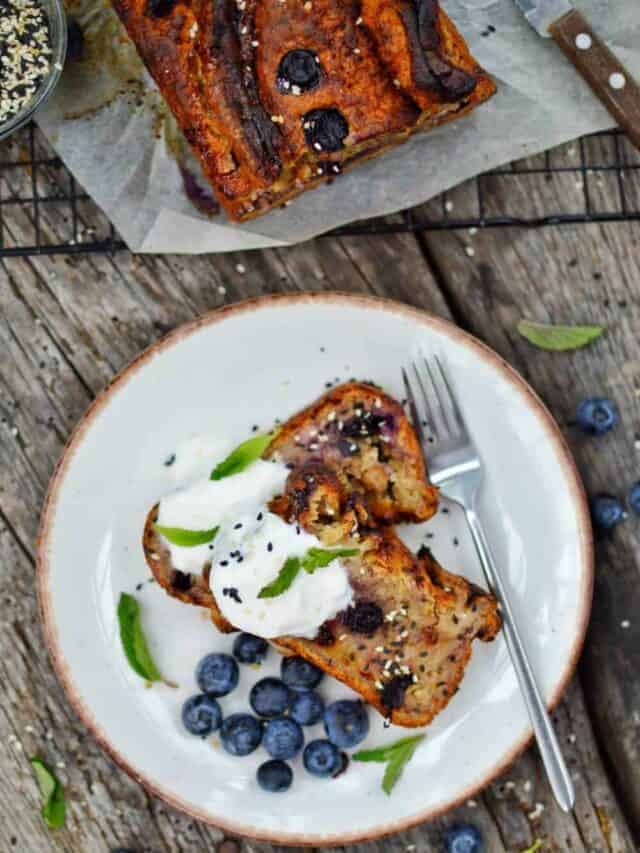 No fuss Blueberry Banana Bread completed with two pieces on a white plate against a dark gray surface