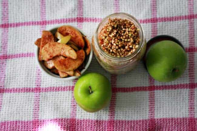 Breakfast groats in a jar next to green apples on a table.