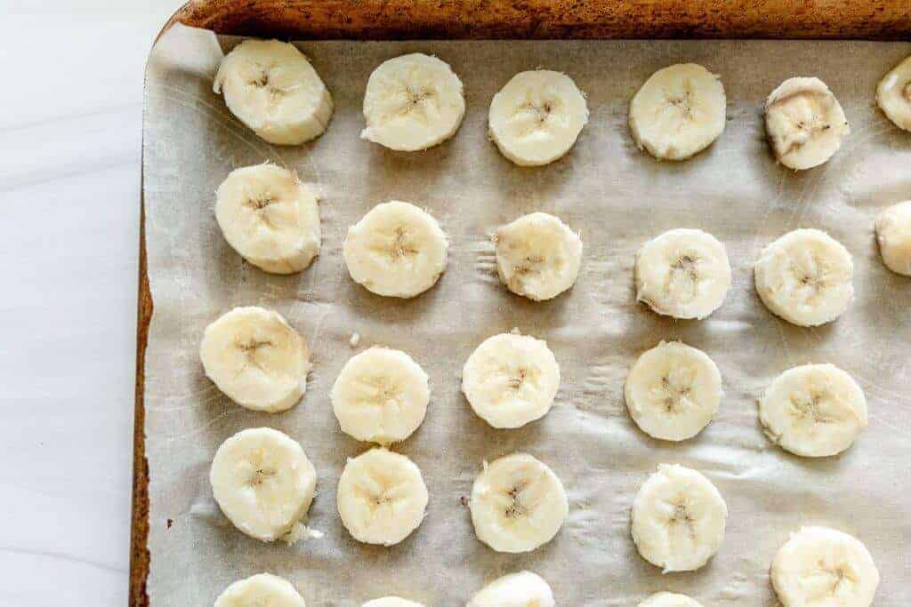 Closeup of frozen banana slices on a parchment-lined baking sheet.