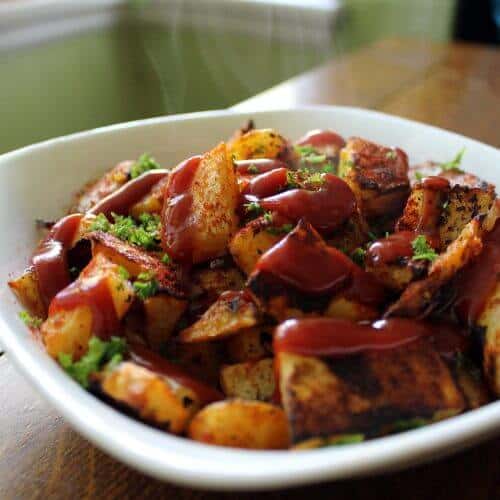 Ketchup coated roasted potatoes in a white bowl.