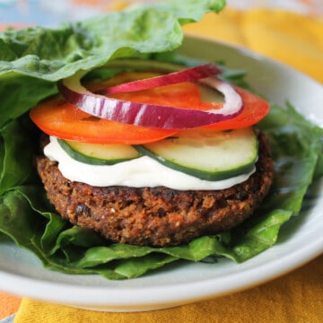 Lentil veggie burger with all the toppings on a bed of lettuce.