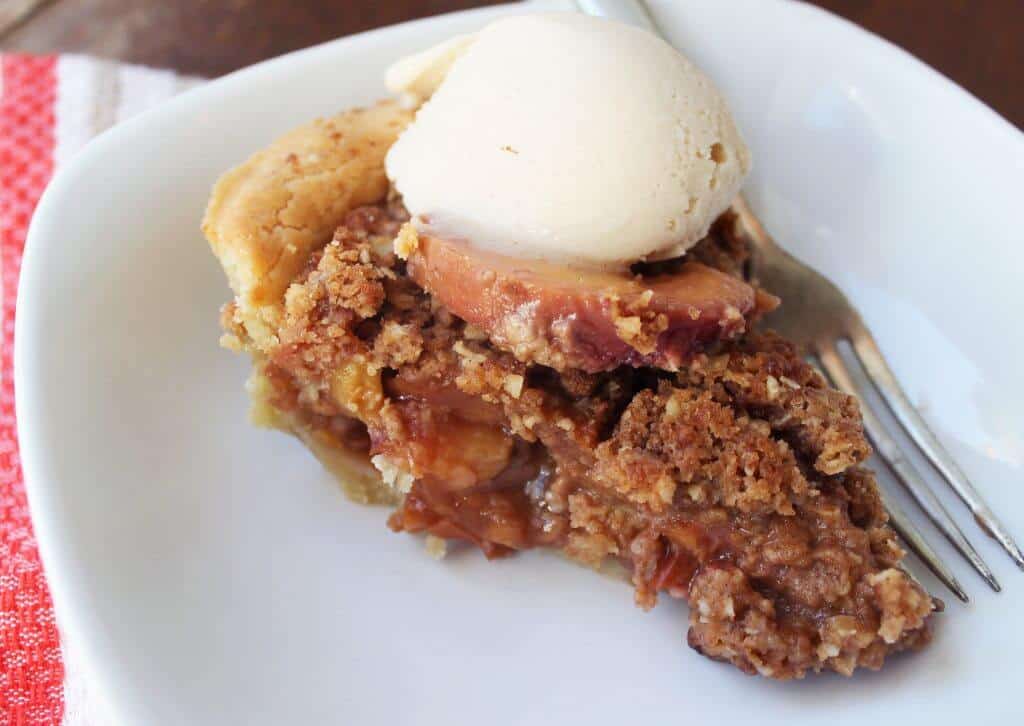 A slice of peach crumb pie topped with a scoop of vanilla ice cream.