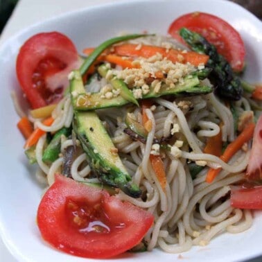 Peanut rice noodles with veggies in a white bowl.