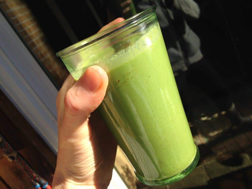 A hand holding a glass of bright jade green smoothie.