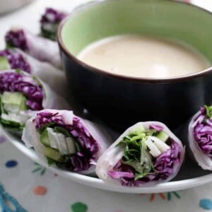 Red cabbage and jicama spring rolls around a cup of sauce.