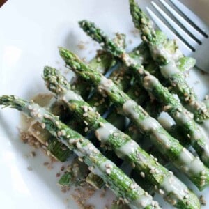 Sesame sauce drenched asparagus on a white plate.