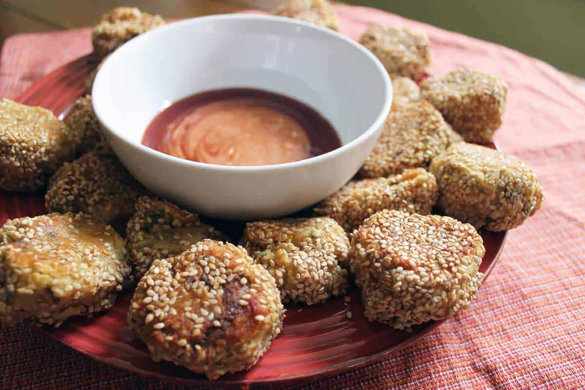 Sesame potato puffs on a plate with a bowl of sauce.