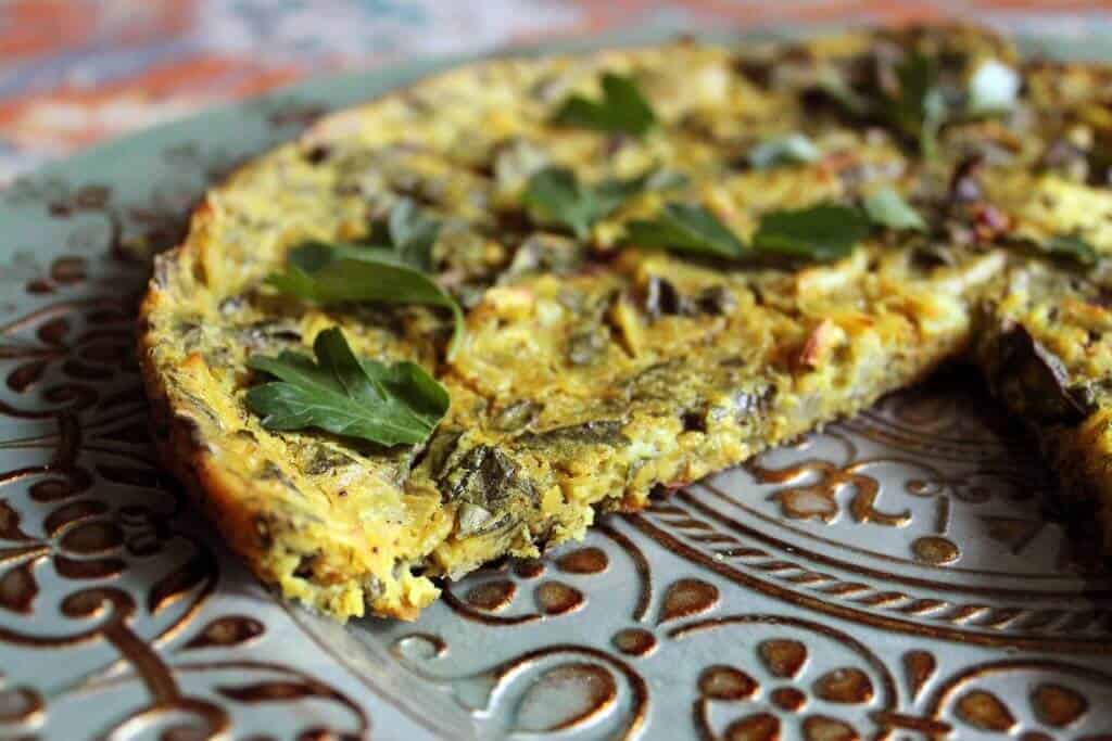 completed vegan frittata on a textured plate with a slice missing