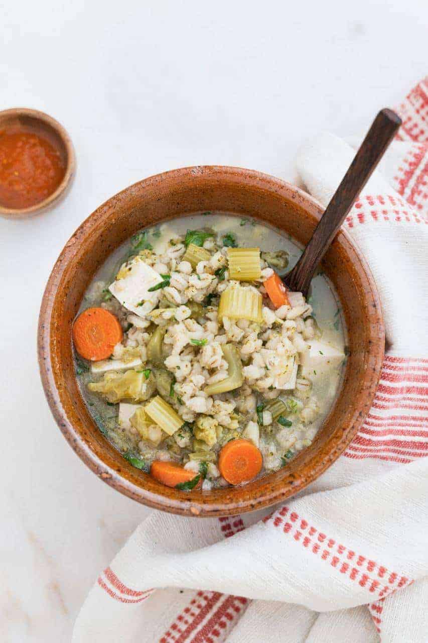 Brown bowl and spoon filled with vegetable barley soup.