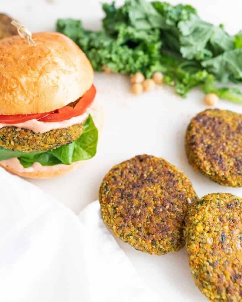 Chickpea Quinoa Burger patties spread out on a white surface with a complete chickpea quinoa burger on the side
