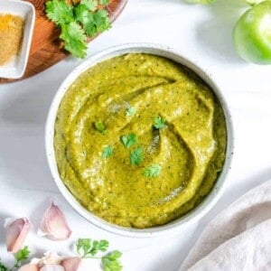 completed Creamy Tomatillo Avocado Salsa Verde in a white bowl against a white background with ingredients in the background