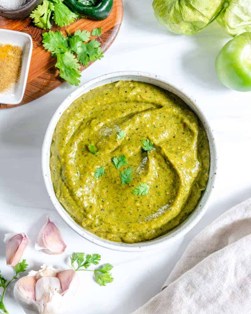 completed Creamy Tomatillo Avocado Salsa Verde in a white bowl with ingredients in the background