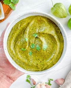 completed Creamy Tomatillo Avocado Salsa Verde in a white bowl with ingredients in the background