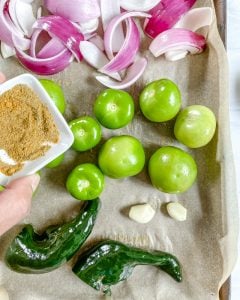 process of adding spices to ingredients in a baking tray with parchment paper