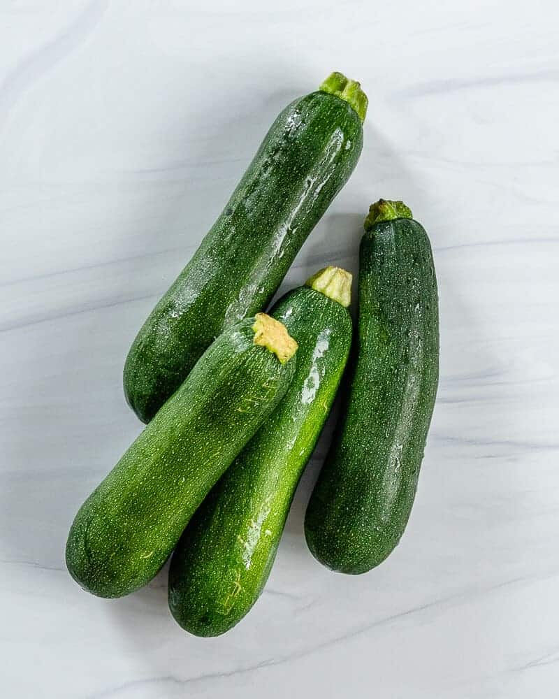 4 raw zucchinis against a white background
