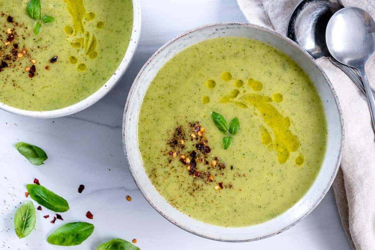 two white bowls of zucchini basil soup in a white background