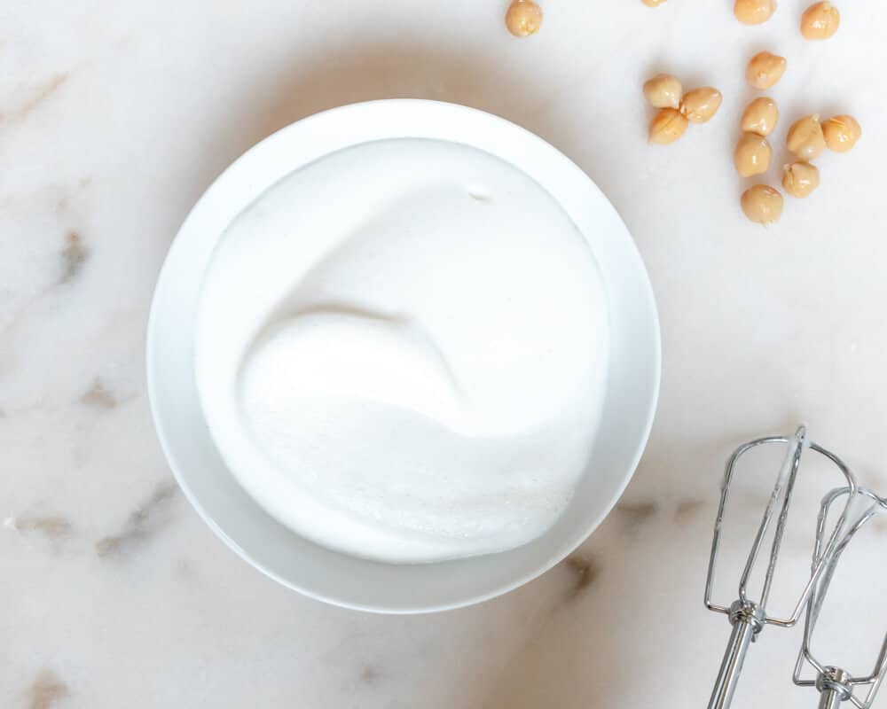 A Bowl of Fluffly Chickpea Brine or Aquafaba with some chickpeas on the side