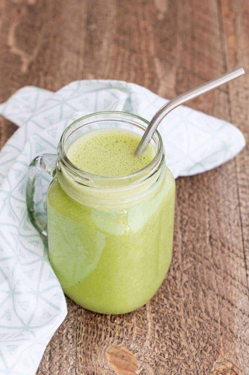 Mason jar with a handle filled with a fresh green smoothie and stainless steel straw.