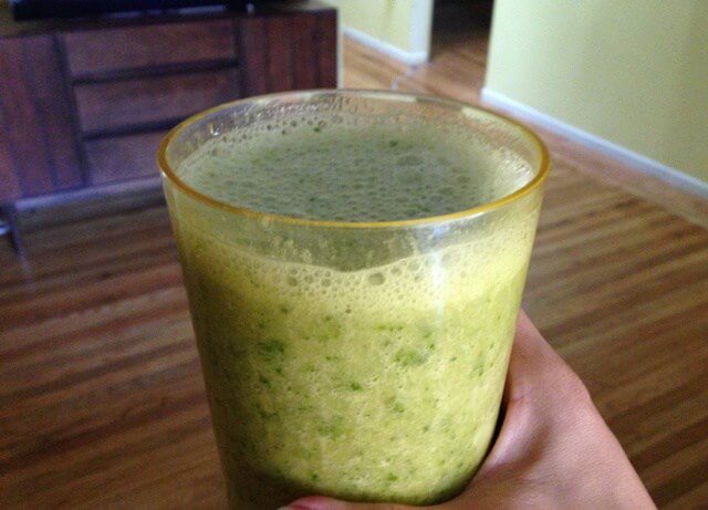 A hand holding a glass of kale and banana smoothie.