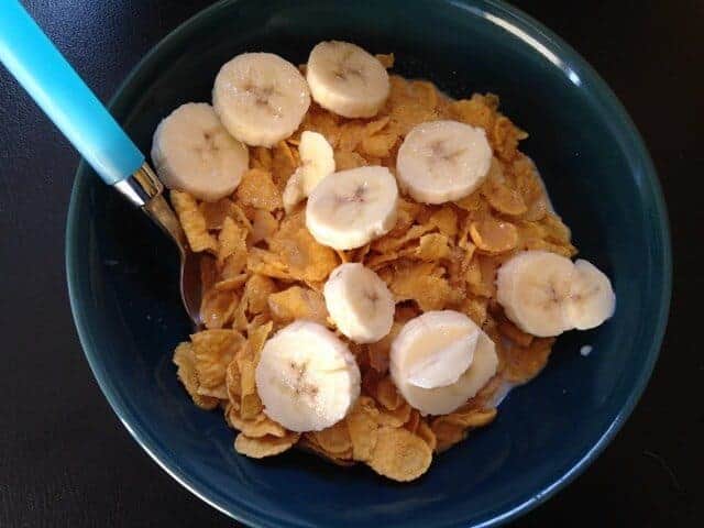 A bowl of cornflakes cereal topped with sliced bananas.