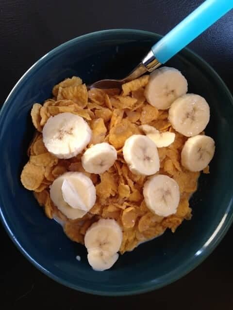 A bowl of cornflake cereal topped with sliced bananas.
