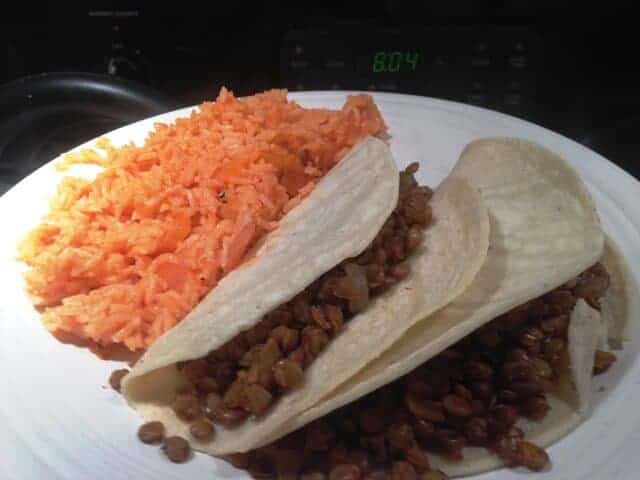 Two vegan tacos and a side of Spanish rice on a white plate.